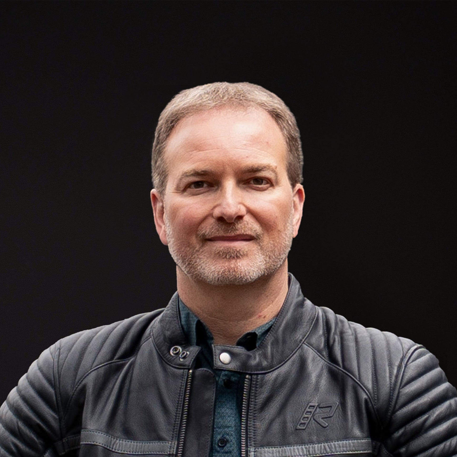 Headshot of Savic Motorcycles CEO Marc Alexander, in a motorcycle jacket against a black background